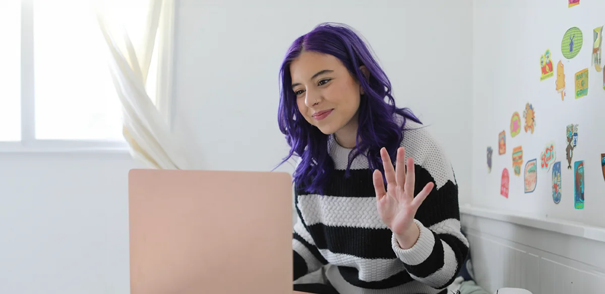Stuednt with purple hair and a stripped sweater attending to an online class
